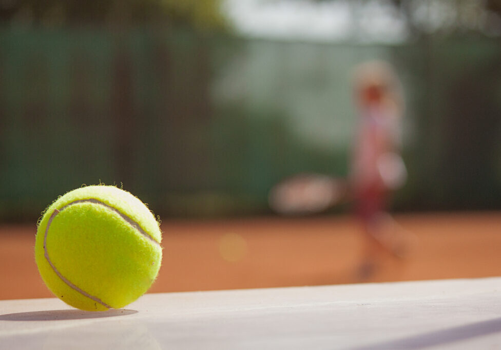 Tennis player in action on tennis court (selective focus, focus on ball in the foreground)